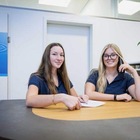 Am Empfang - Zwei Personen sitzen am Tisch und entnehmen einen Anruf entgegen