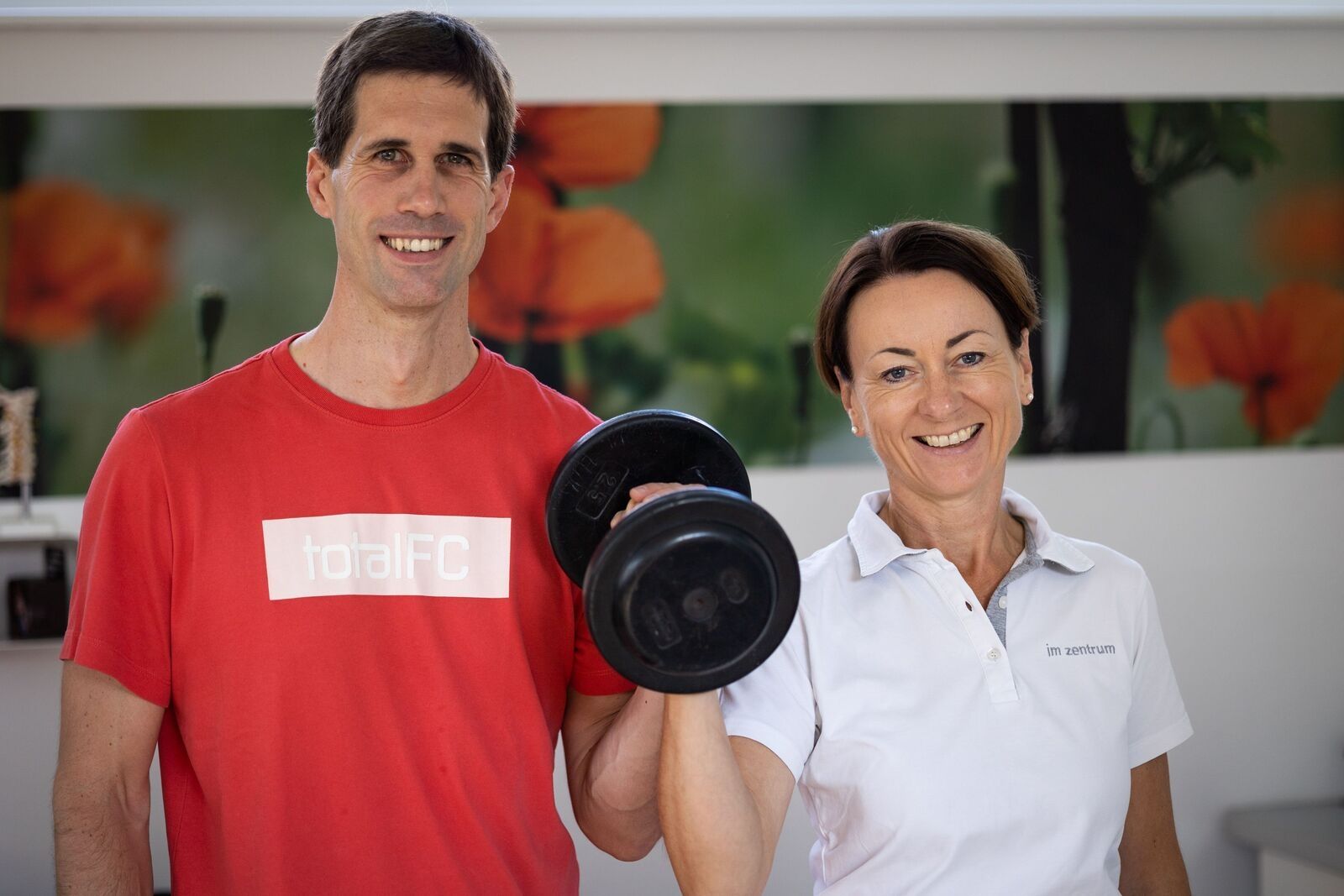 Physiotherapeuten halten zusammen eine Hantel hoch